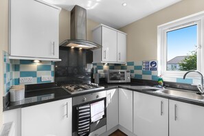 A modern kitchen with white cabinets, a gas stove, a microwave, and a window with a view. - Heathrow Living Apt. 08 by 360 Stays (Stanwell)