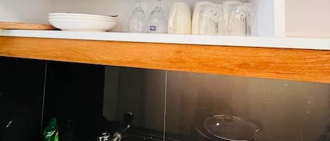 Une cuisine avec des meubles en bois, un évier en acier inoxydable, une casserole sur la cuisinière et une étagère avec de la verrerie et des assiettes.