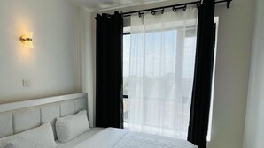 A bedroom with a bed, a wall-mounted light, a window with curtains, and a view outside. - Fabulous 1-bedroom apartment (Nairobi)