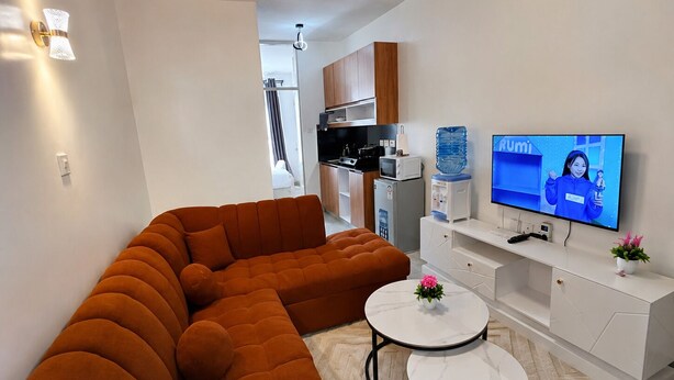 A modern living room with a sectional sofa, a flat-screen TV, a small coffee table, and a water dispenser. - Fabulous 1-bedroom apartment (Nairobi)