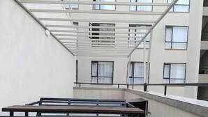 A multi-level outdoor terrace with a metal railing, benches, and a view of a building with multiple windows. - Fabulous 1-bedroom apartment (Nairobi)