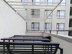 A multi-level outdoor terrace with a metal railing, benches, and a view of a building with multiple windows. - Fabulous 1-bedroom apartment (Nairobi)