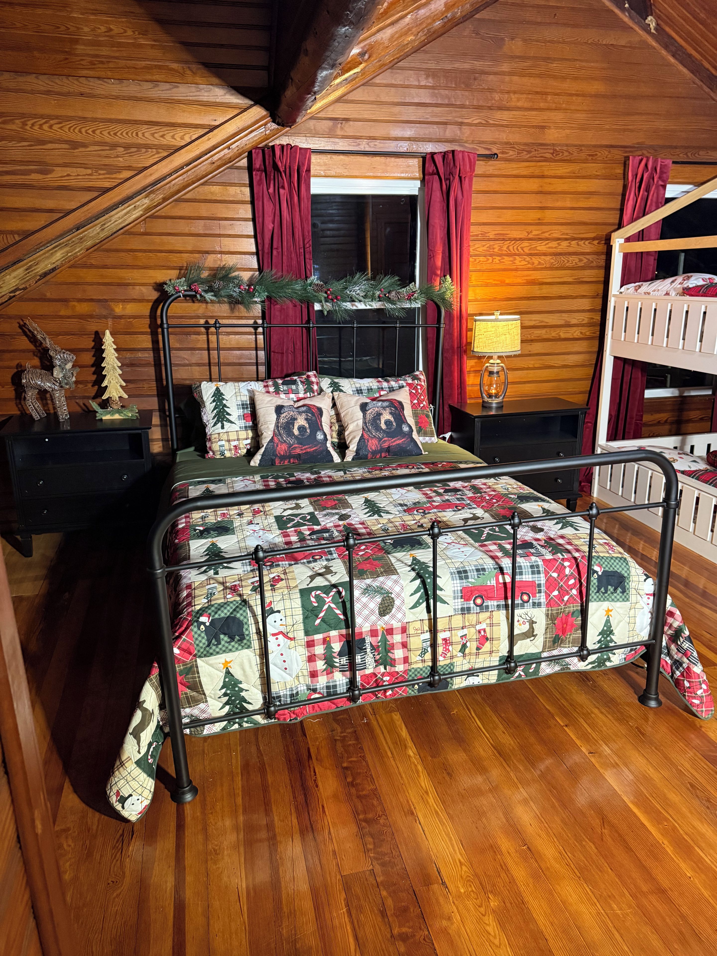 A wooden cabin bedroom with a bed, a nightstand, a lamp, and a bunk bed.