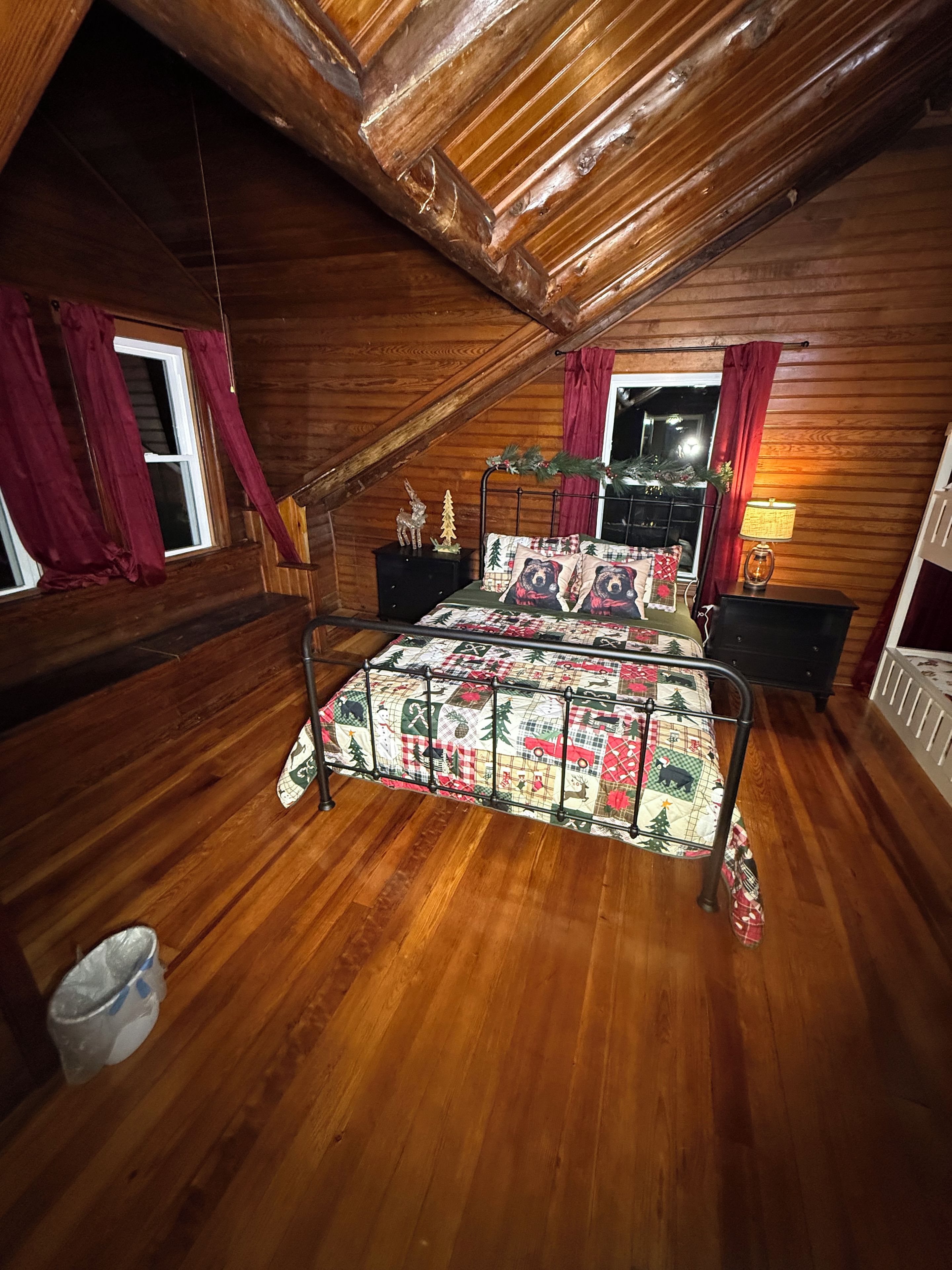 Una camera da letto con soffitto in legno, un letto con copriletto, due comodini, una finestra con tende e un comodino con una lampada.
