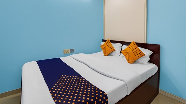 A hotel room with a bed, a nightstand, and a wall-mounted light fixture. - Dev Hotel Mansarovar (Jaipur)