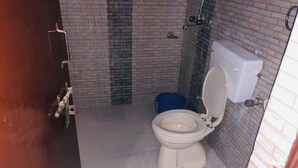 A bathroom with a toilet, a blue bucket, and a shower. - Dev Hotel Mansarovar (Jaipur)