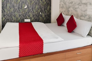 A bed with a white and red bedspread, two red pillows, and a wooden headboard. - Dev Hotel Mansarovar (Jaipur)