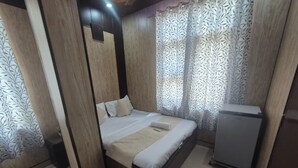 A bedroom with a bed, a small refrigerator, and patterned curtains. - Dev Hotel Mansarovar (Jaipur)