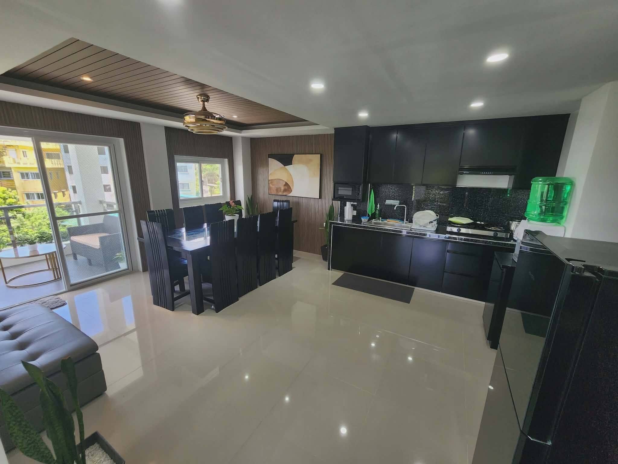 A modern kitchen with black cabinets, a dining area with a black table and chairs, and a view of a building outside.