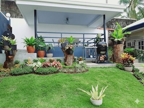 Una casa moderna con césped cuidado, plantas en macetas y una parrilla.