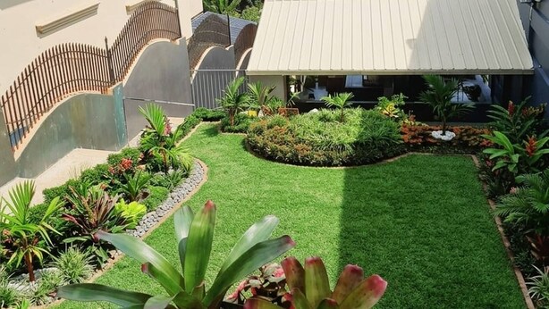 Propiedad residencial con césped cuidado, un patio cubierto y vistas a un paisaje verde exuberante con palmeras.