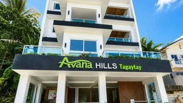 Un hotel de varios pisos llamado 'Avana Hills Tagaytay' con un diseño arquitectónico moderno, que cuenta con balcones y una escalera que conduce a la entrada.