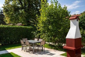 Eine Terrasse im Freien mit Tisch und Stühlen, umgeben von Grünpflanzen und einer rot-weißen Struktur.