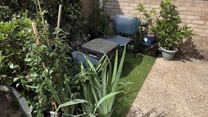Ein Gartenbereich mit einem kleinen Tisch und Stühlen, Blumentöpfen und einer Hecke.