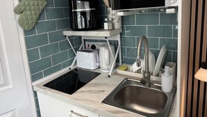 Eine kompakte Küche mit Mikrowelle, Toaster, Spüle und einer Edelstahl-Dunstabzugshaube.