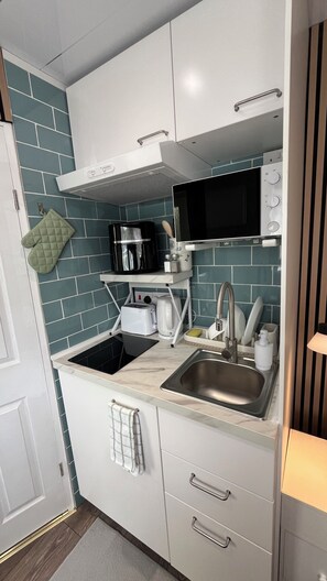 A compact kitchen with a microwave, toaster, sink, and a stainless steel range hood. - Stylish Micro-Apartment with Secure Parking – Fast Train to London Central (Slough)