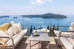 Eine Terrasse mit Meerblick, ein Tisch mit einem Hut und eine Schüssel Obst.
