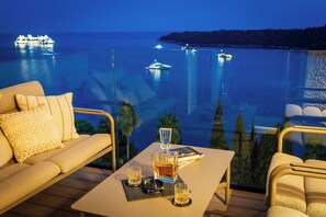 Ein Balkon mit einer Couch, einem Tisch mit Gläsern und einer Flasche, und Blick auf das Meer mit Booten.