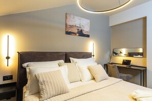 Ein Hotelzimmer mit einem Bett, Nachttischlampen, einem Schreibtisch mit einem Laptop und einem Bild an der Wand.