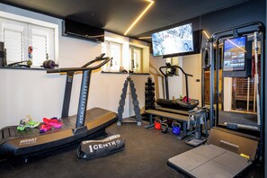 Une salle de sport à domicile équipée d’un tapis de course, d’un banc de musculation, d’haltères et d’un écran de télévision.