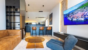 A modern living room with a leather sofa, a blue armchair, a glass coffee table, and a kitchen in the background.