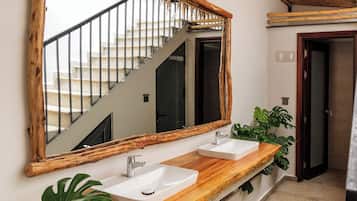 Un baño con tocador de madera, dos lavamanos, un espejo grande y una escalera que sube a un nivel superior.