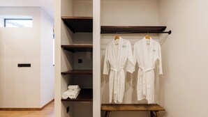Un vestidor con estantes de madera, un banco y dos batas blancas colgadas de ganchos.