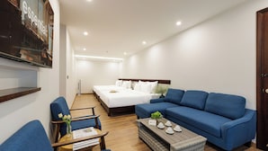 A modern hotel room with a large bed, a blue sofa, a small table with a vase of flowers, and a flat-screen TV mounted on the wall.