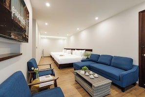 A modern hotel room with a large bed, a blue sofa, a small table with a vase of flowers, and a flat-screen TV mounted on the wall.