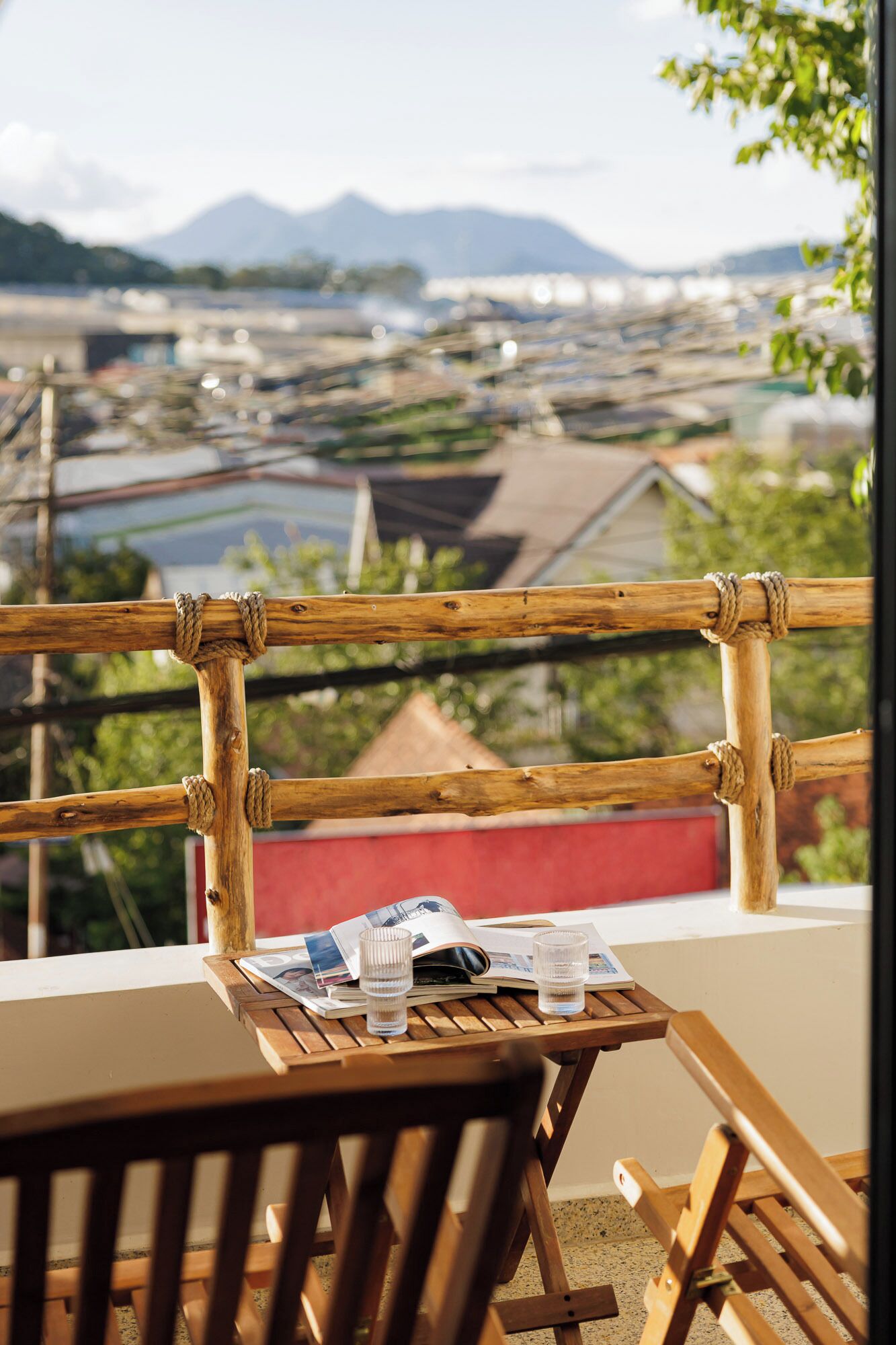 A wooden table with a magazine and glasses, overlooking a coastal cityscape with mountains in the distance.