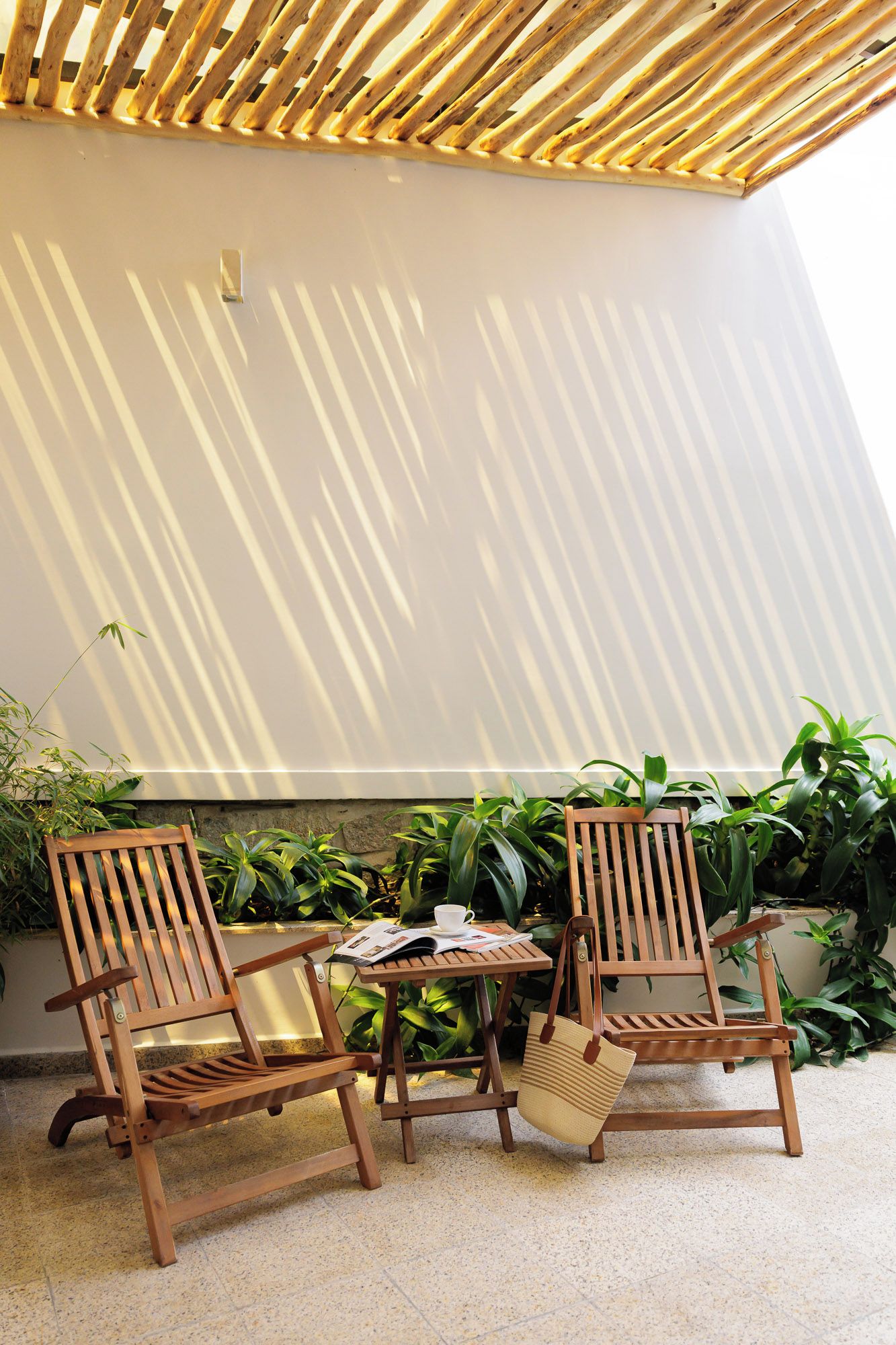 Un espace extérieur aménagé avec des meubles en bois, comprenant deux chaises et une table, le tout entouré de plantes en pot.