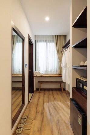 Un pasillo con suelo de madera, un banco, una ventana con cortinas, un espejo y un zapatero.