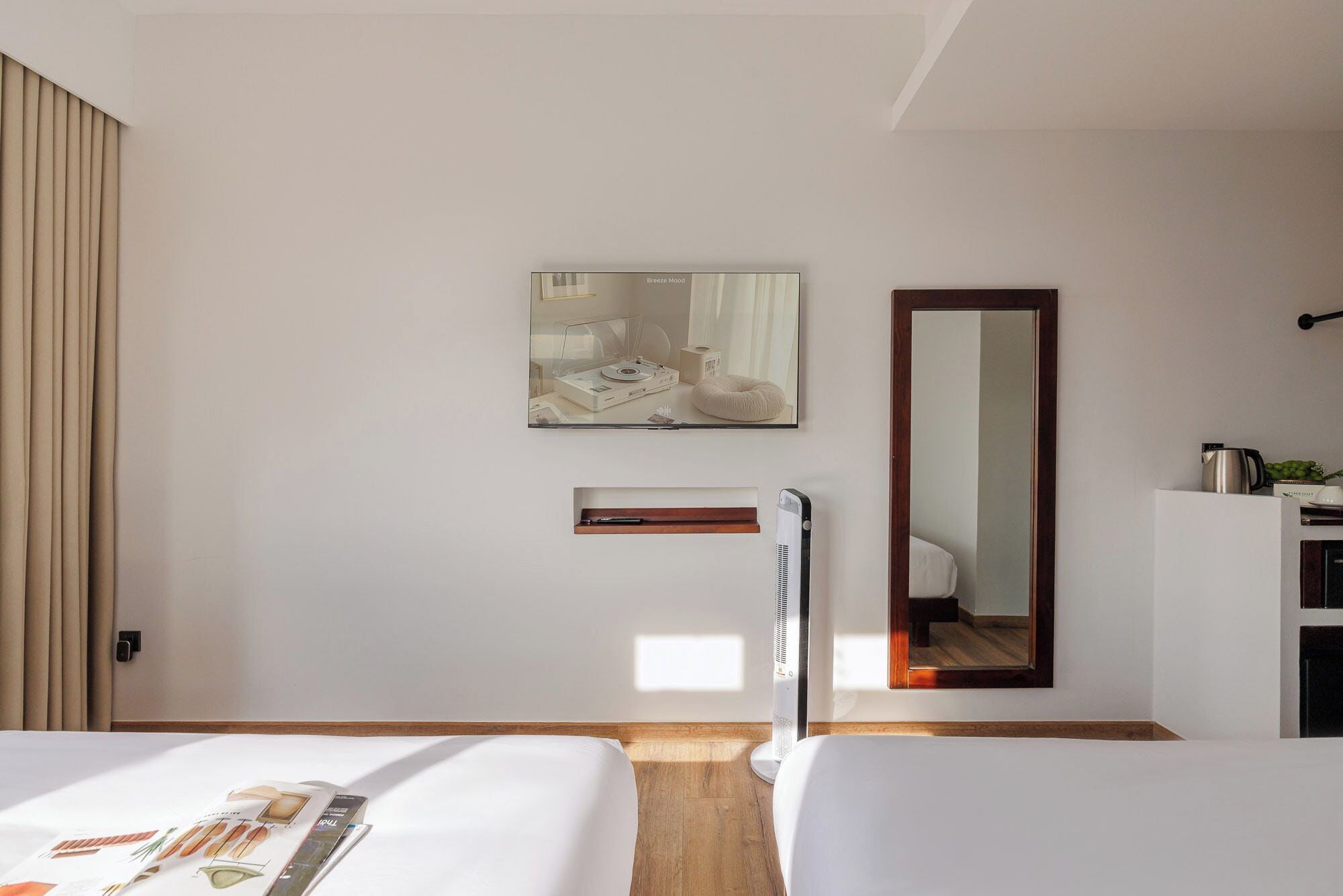 Habitación de hotel con dos camas, un espejo grande, una obra de arte en la pared y un estante pequeño.