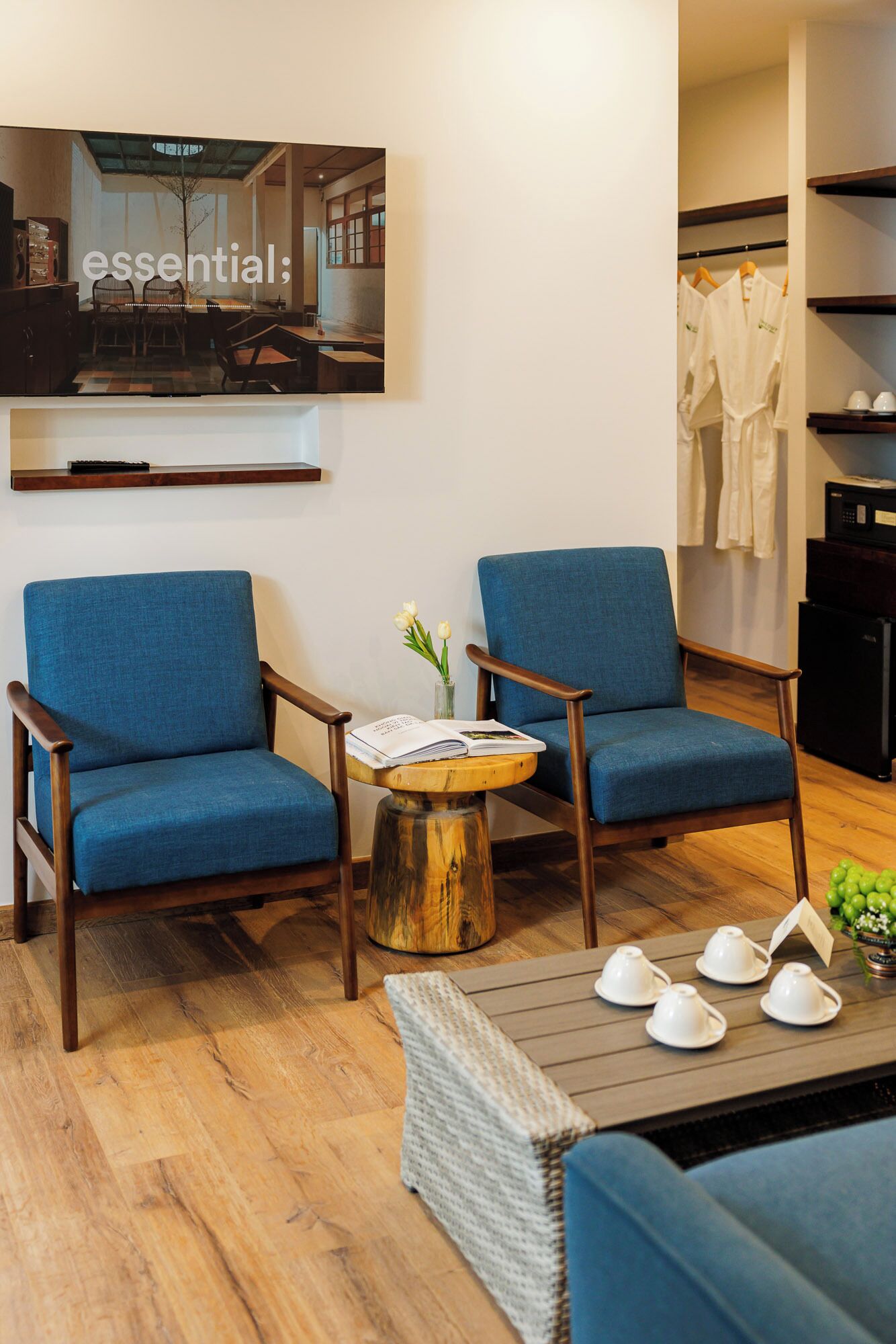 A room with two blue armchairs, a small wooden table with a book and flowers, and a coffee table with teacups.