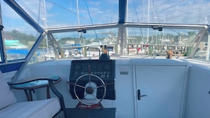 A boat's cockpit with a steering wheel, control panel, and seating area.