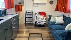 A compact living space with a kitchenette, a blue sofa, a chair with a nautical theme, and a wooden floor.