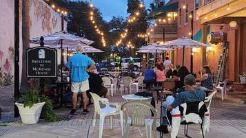 An outdoor seating area with tables and chairs, string lights overhead, and a sign for 'Breezeway to McKenzie House.'