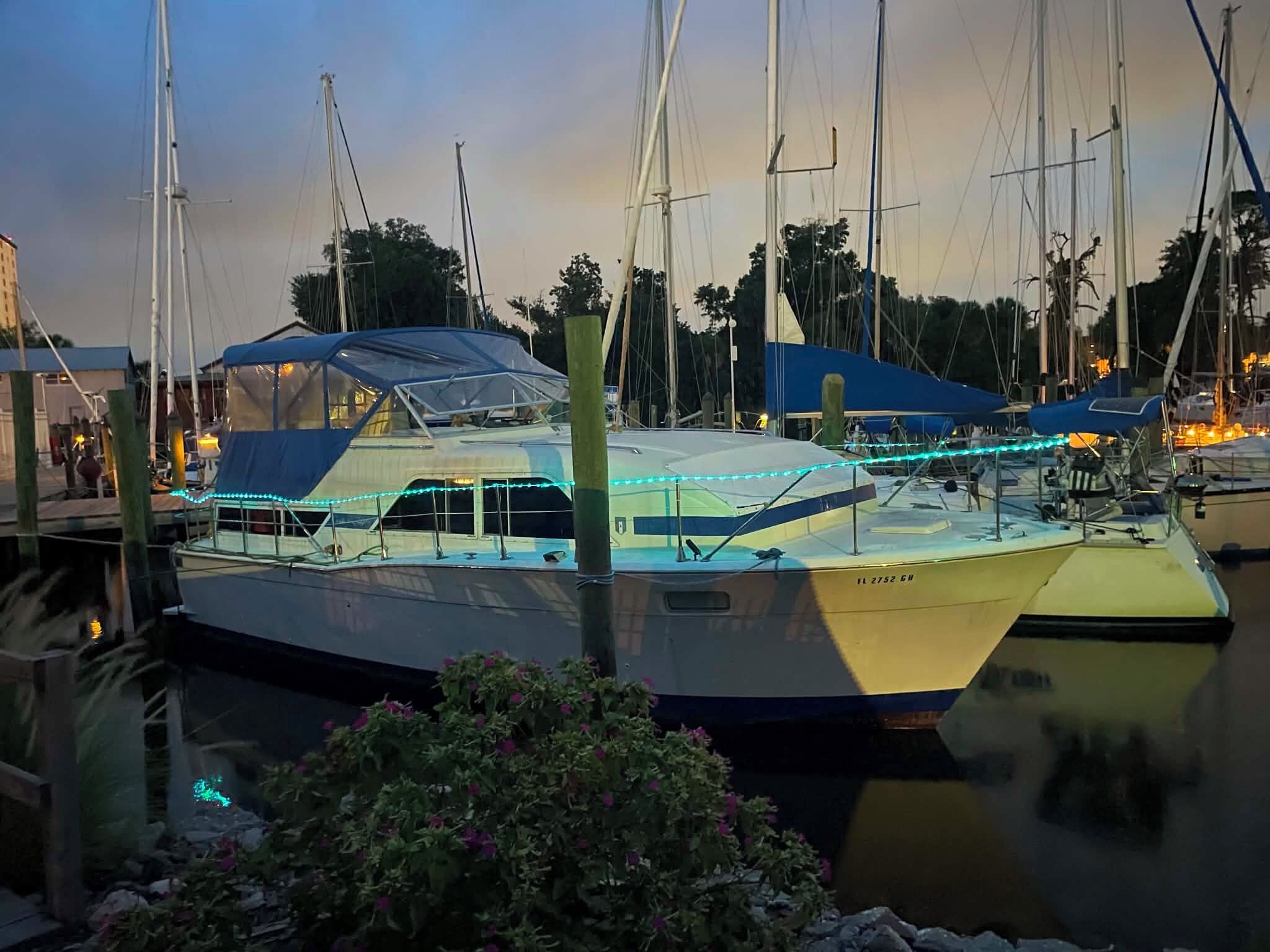 Een jachthaven met verschillende boten afgemeerd, waaronder een zeiljacht met een overdekt dek en blauwe verlichting.