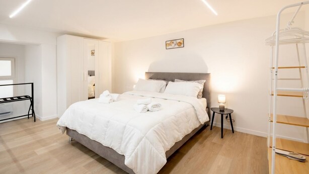 A neatly made bed with white bedding, a bedside table with a lamp, a white wardrobe, and a ladder against the wall. - ALL Casa Di Lu – Chic 2-Bedroom Stay for 7 in Bari (Bari)