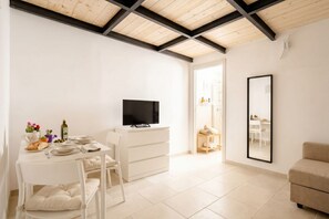 Ein moderner, gut beleuchteter Raum mit einem Esstisch für zwei Personen, einem Flachbildfernseher und einem großen Spiegel an der Wand.