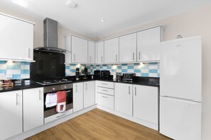 A modern kitchen with white cabinets, a black countertop, and a blue and white backsplash. - Heathrow Living 2BDR 2BA Apt 09-360stays (Stanwell)