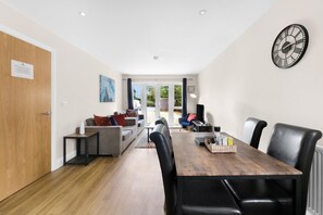 A modern living room with a wooden dining table, black leather chairs, a grey sofa, and a large wall clock. - Heathrow Living 2BDR 2BA Apt 09-360stays (Stanwell)