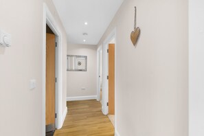 A hallway with wooden flooring, white walls, and a ceiling light. - Heathrow Living 2BDR 2BA Apt 09-360stays (Stanwell)