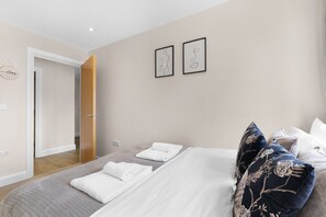 A bedroom with a bed, two framed artworks, a door, and a wall-mounted light fixture. - Heathrow Living 2BDR 2BA Apt 09-360stays (Stanwell)