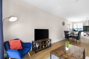 A modern living room with a blue sofa, a wooden coffee table, and a flat-screen TV. - Heathrow Living 2BDR 2BA Apt 09-360stays (Stanwell)