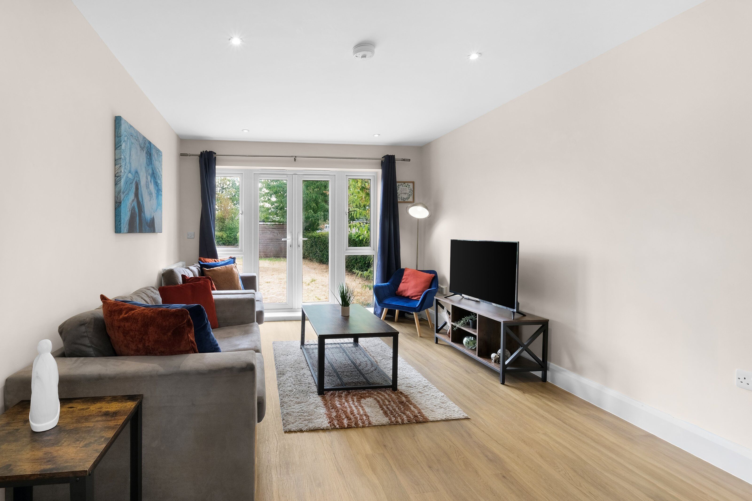 Uma sala de estar moderna com sofá, mesa de centro, TV e vista para o exterior através de portas de vidro.