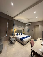 Una habitación de hotel moderna con cama, mesita de noche, silla, escritorio y unidad de aire acondicionado.
