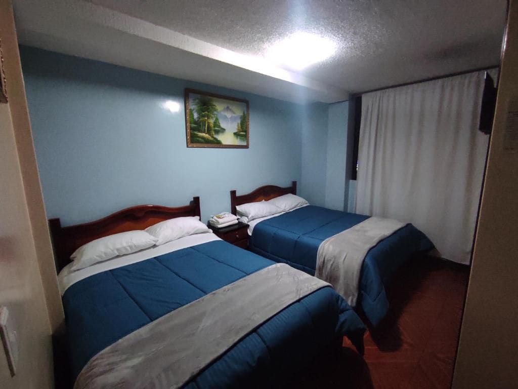 Ein Hotelzimmer mit zwei Betten, einem Nachttisch, einem Bild an der Wand und einem Fenster mit Vorhängen.