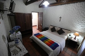 A bedroom with a bed, bedside table, lamp, and a door leading to another room. - Hostal bolaris (Quito)