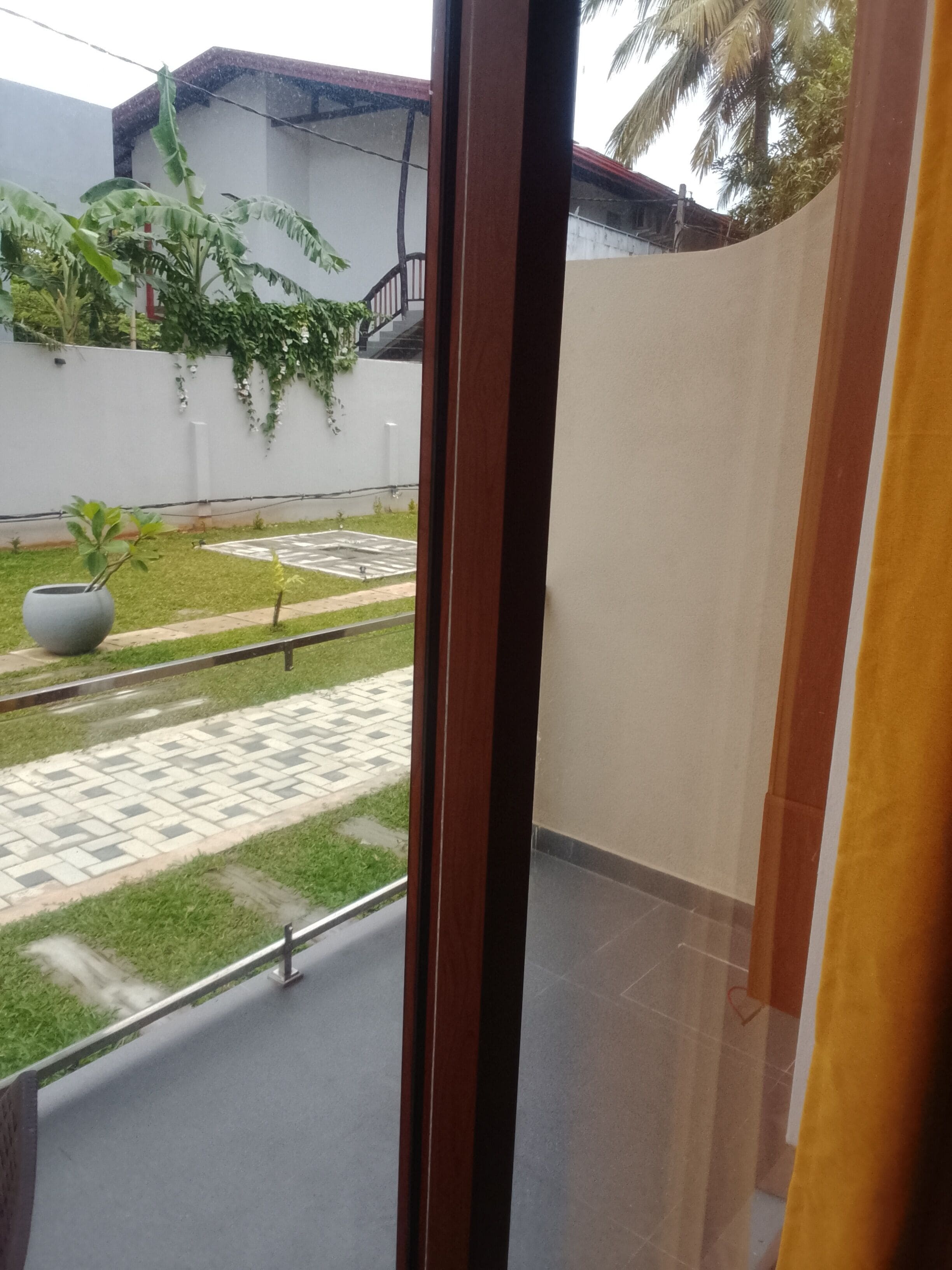 Vista desde un balcón con zona pavimentada, planta en maceta y pared blanca con escalera.